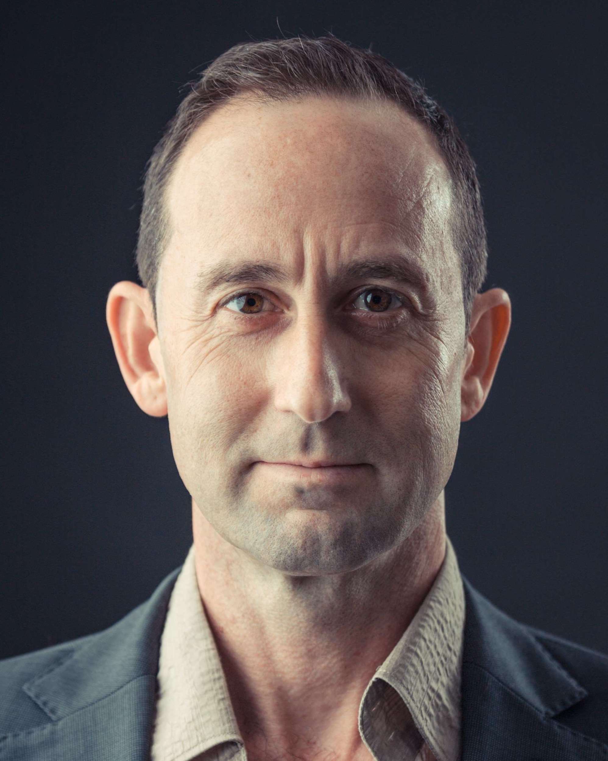 Man wearing a dark jacket over a light shirt against a black background